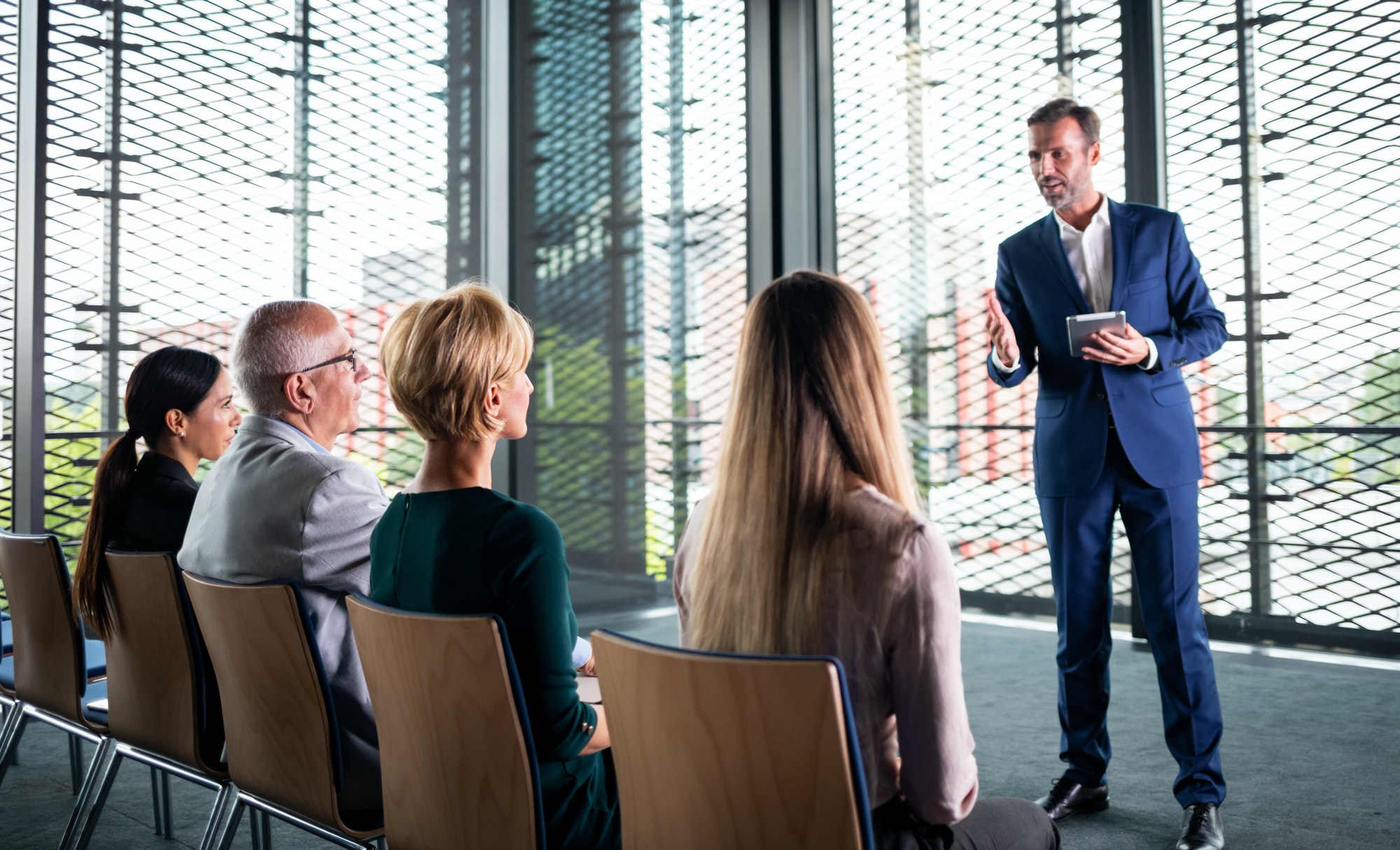 Business coach gesturing with hand while group of people sitting at the chairs in front of him